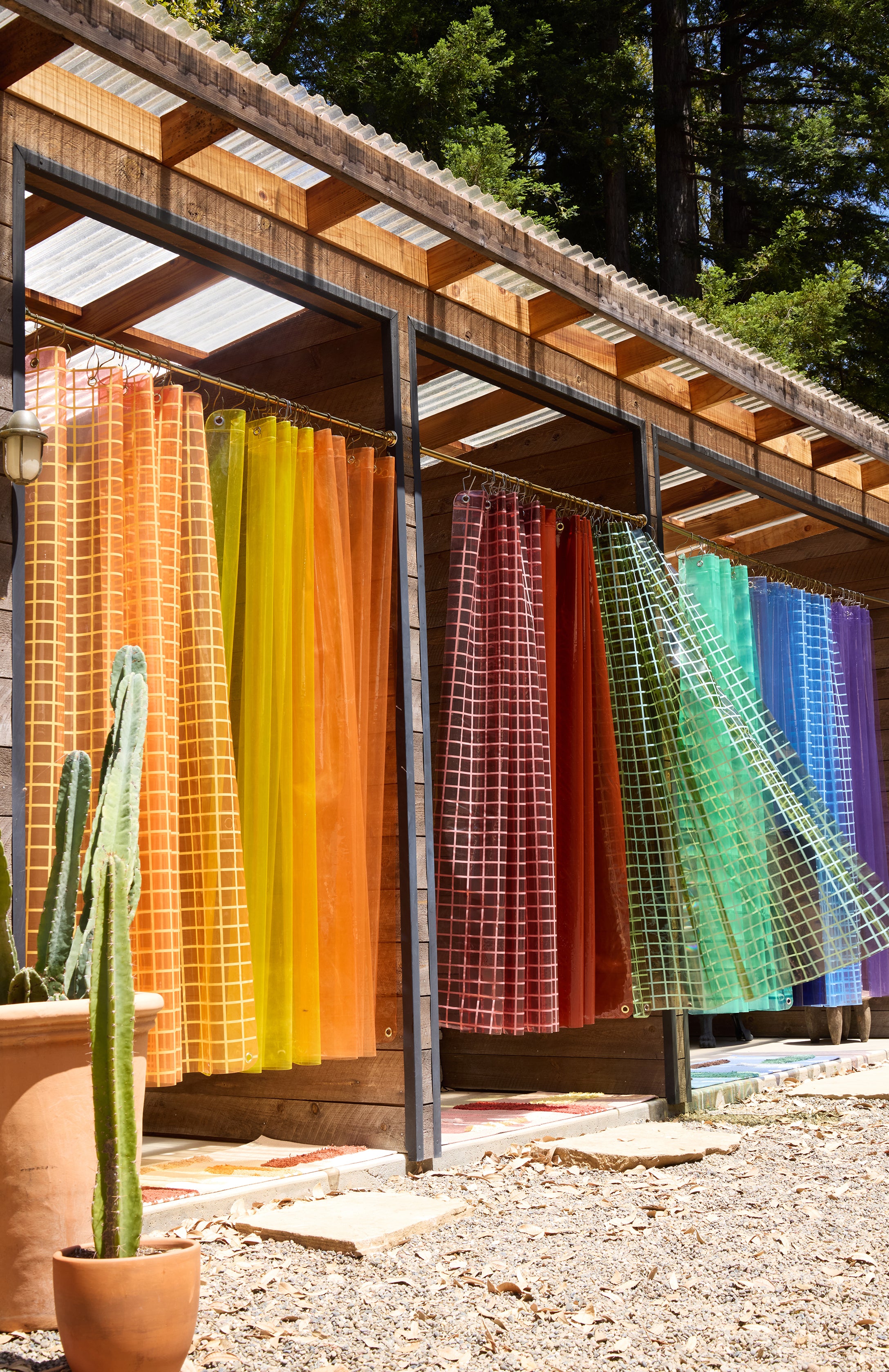 Colorful fabric panels hanging outdoors on a wooden structure with cacti in the foreground.