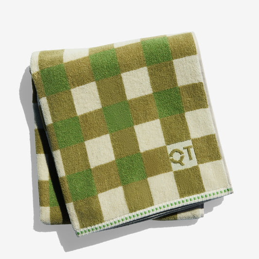 Folded checkered towel with green and beige squares and a logo on a white background