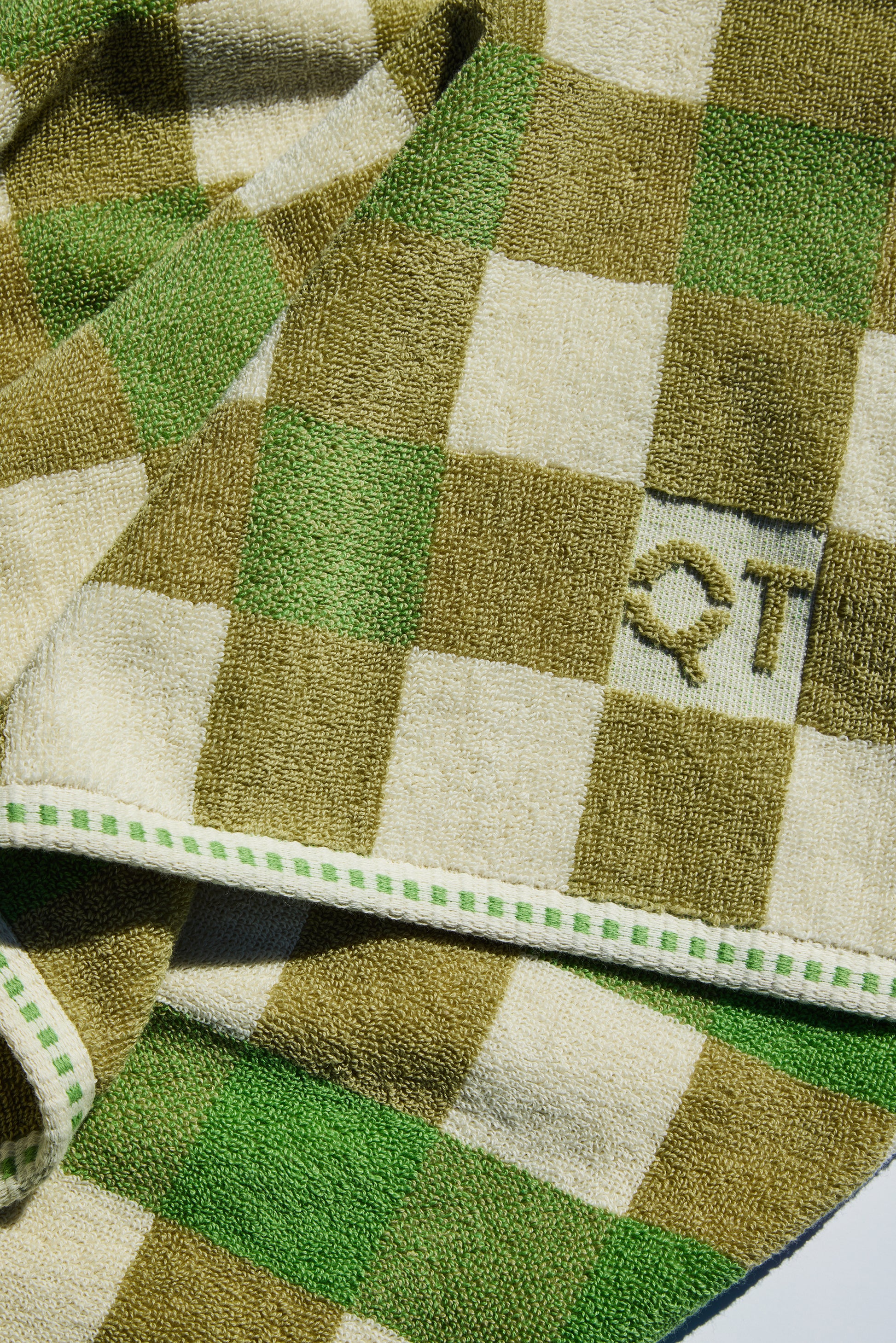 Checkered towel with green and beige pattern and 'QT' logo.