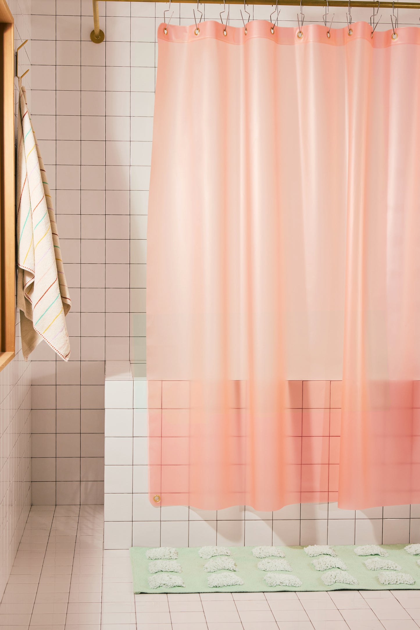 A peach-pink shower curtain hanging in a tiled bathroom, with a matching pale green bath mat on the floor and a striped towel hanging on the left.