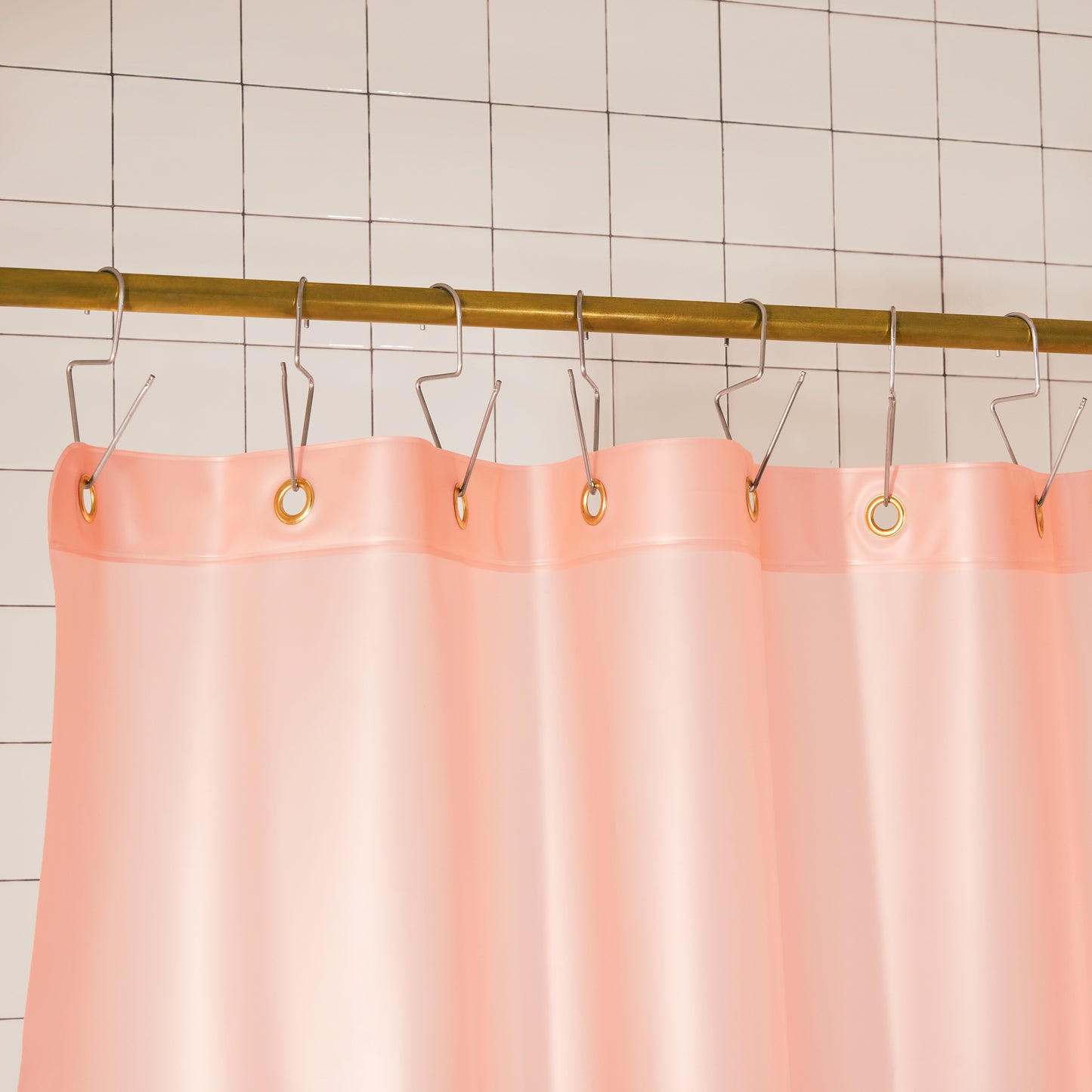 A peach pink shower curtain hanging from a gold metal rod with silver hooks against a white tiled wall.