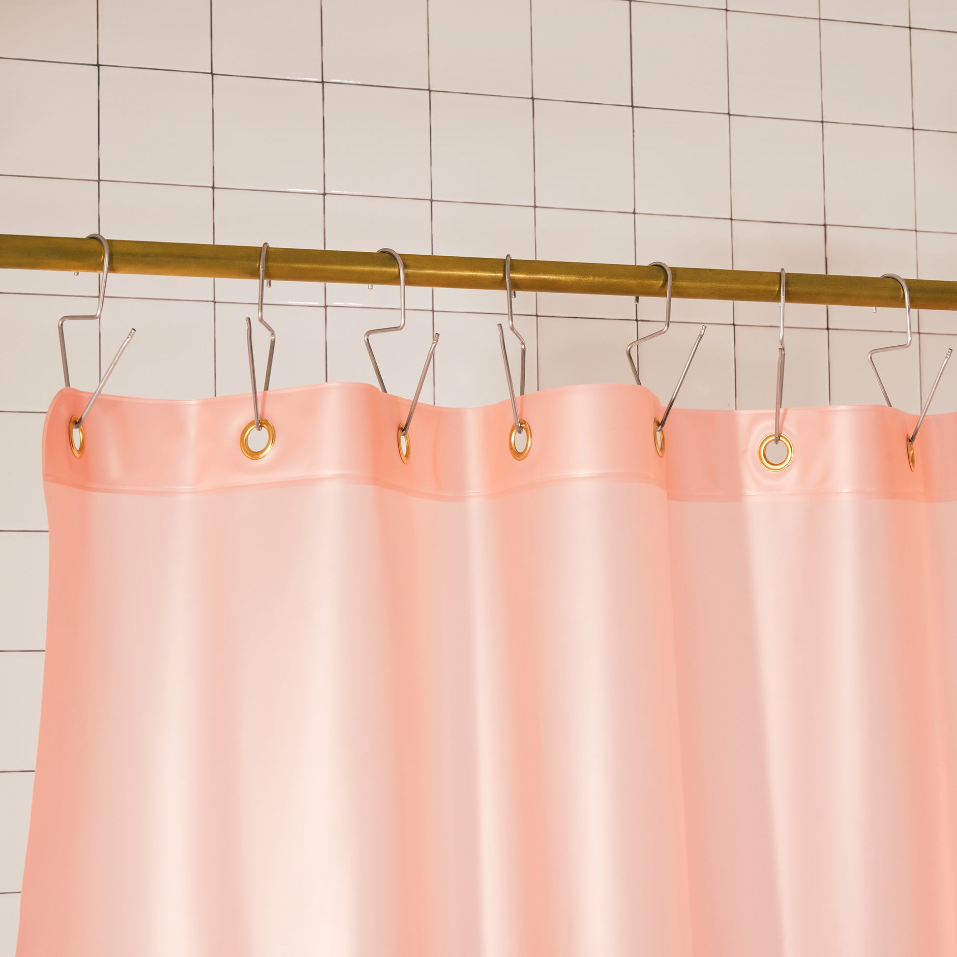 A peach pink shower curtain hanging from a gold metal rod with silver hooks against a white tiled wall.