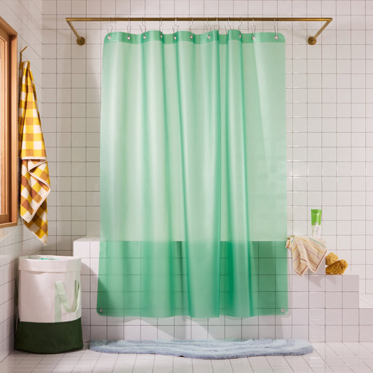 A mint green shower curtain hanging in a tiled bathroom next to a yellow-and-white checkered towel and a white hamper.