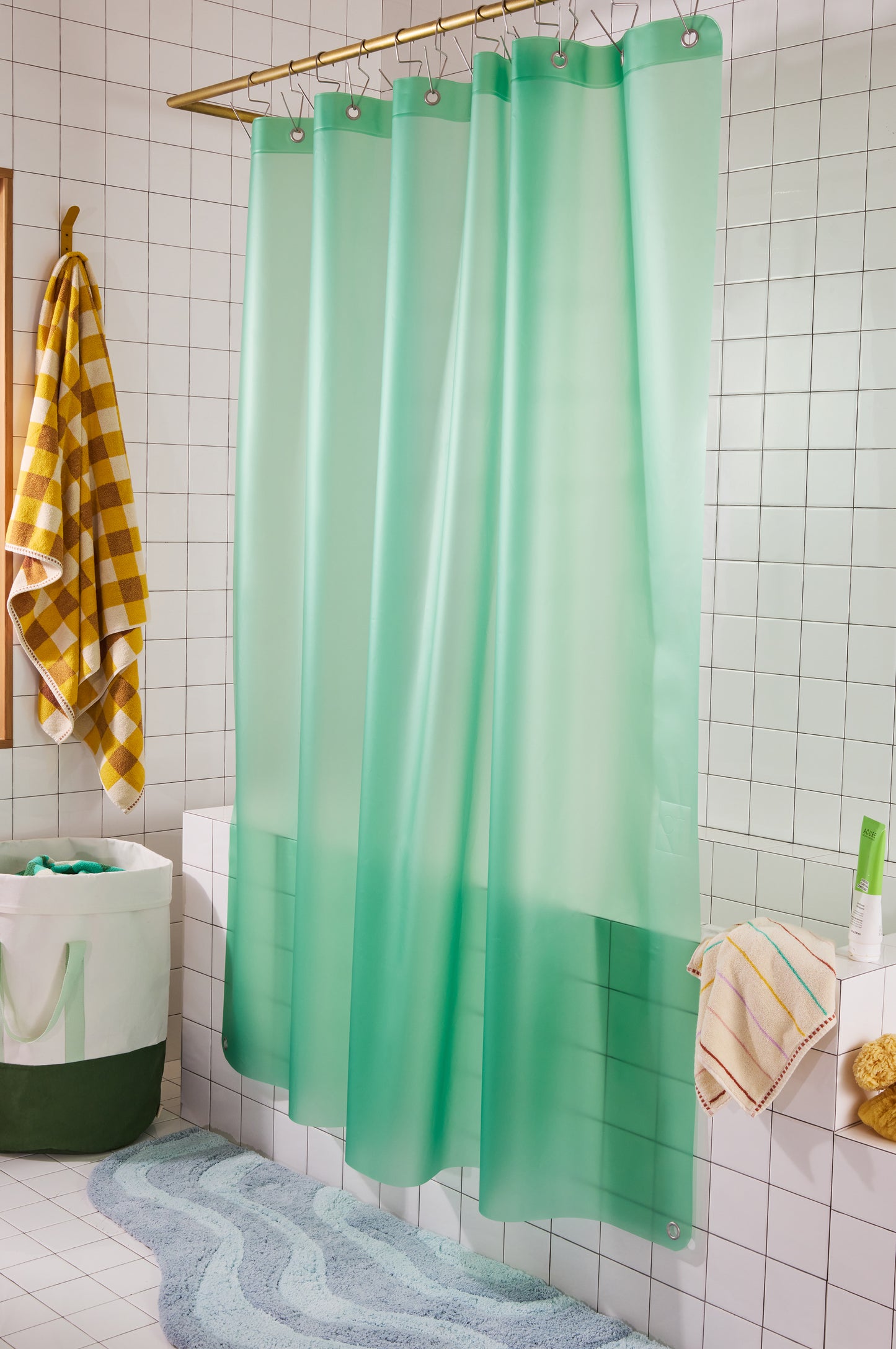 green shower curtain with yellow and white checkered towel in a white tiled bathroom. 
