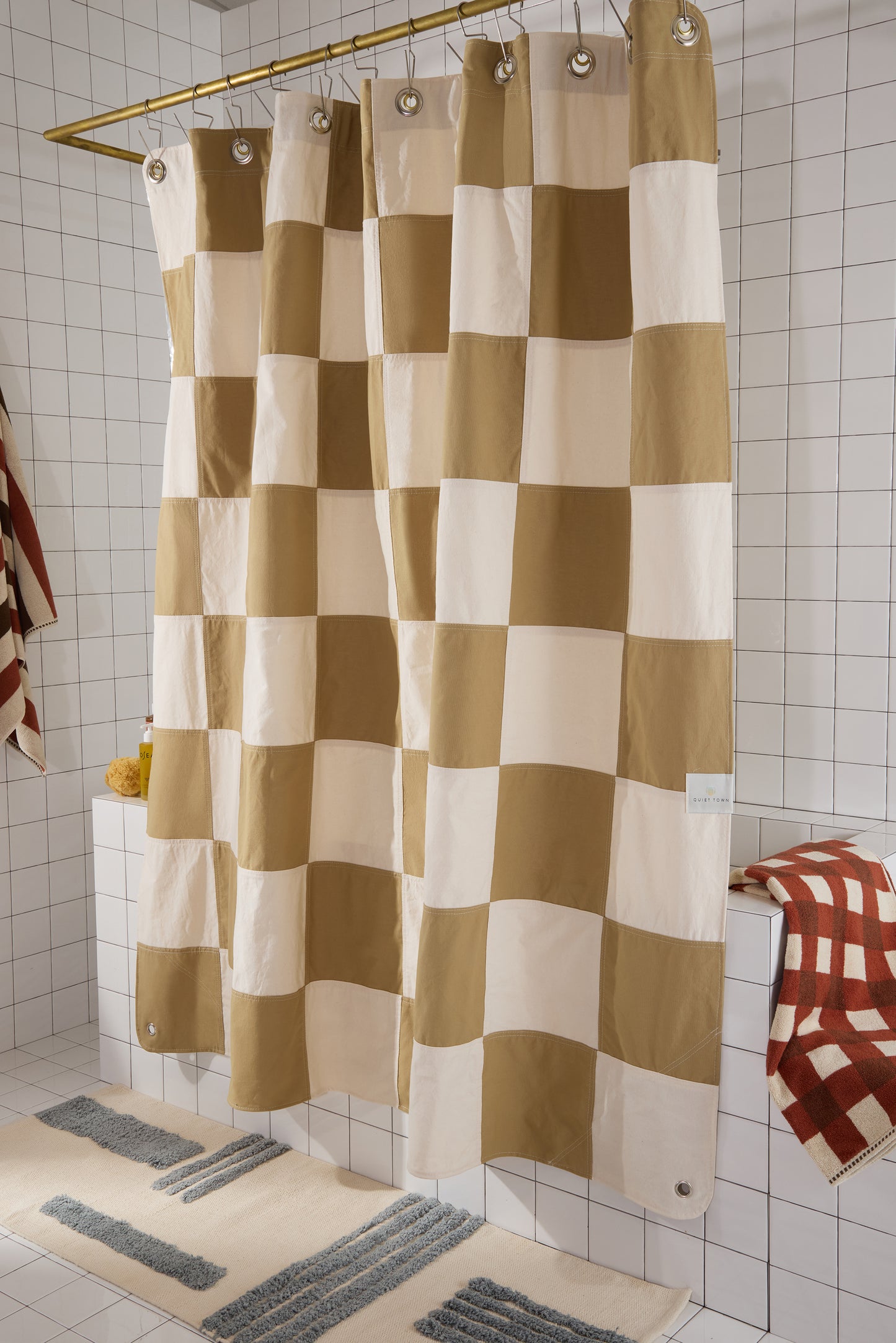 checkered shower curtain in tiled bathroom with rug and patterned towels. 