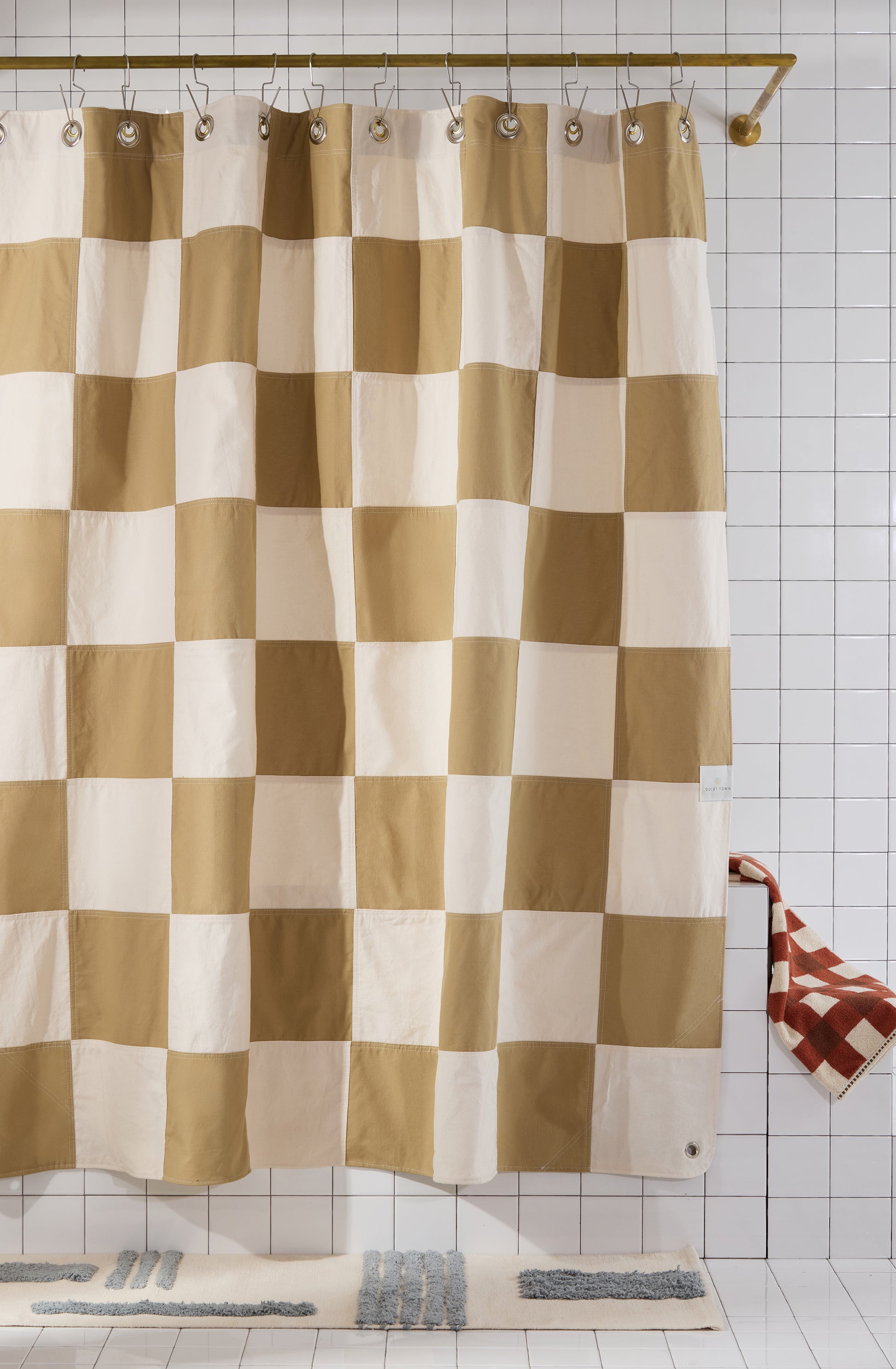 checkered shower curtain hanging in tiled bathroom with rug and towel. 