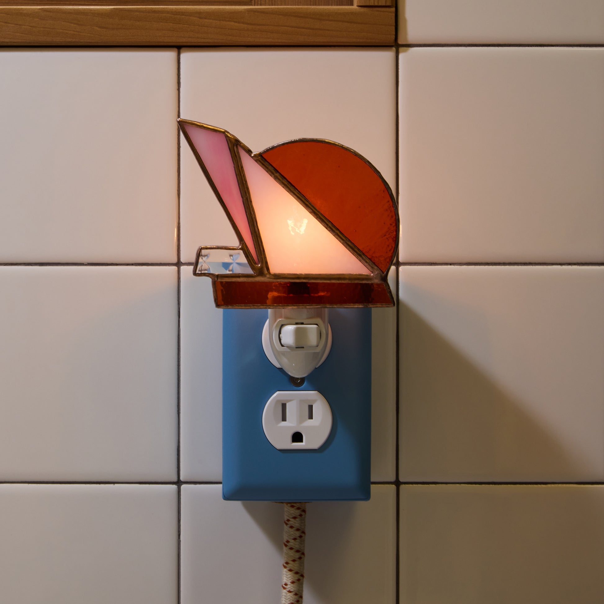 Decorative night light with stained glass design on a tiled wall.