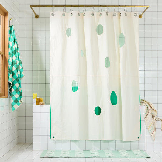 cream curtain with circles cut out and green liner behind it on white tiled bathroom set. 