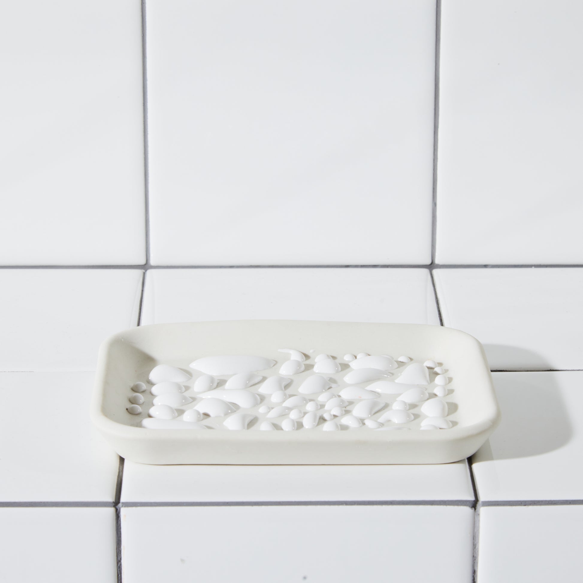 White textured soap dish shot in white tiled bathtub. 