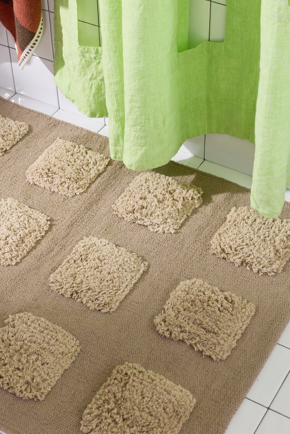 Close-up of the brown/taupe, natural bath runner showing its textured woven base and raised plush tufted squares in warm neutral shades beneath a lime green shower curtain.