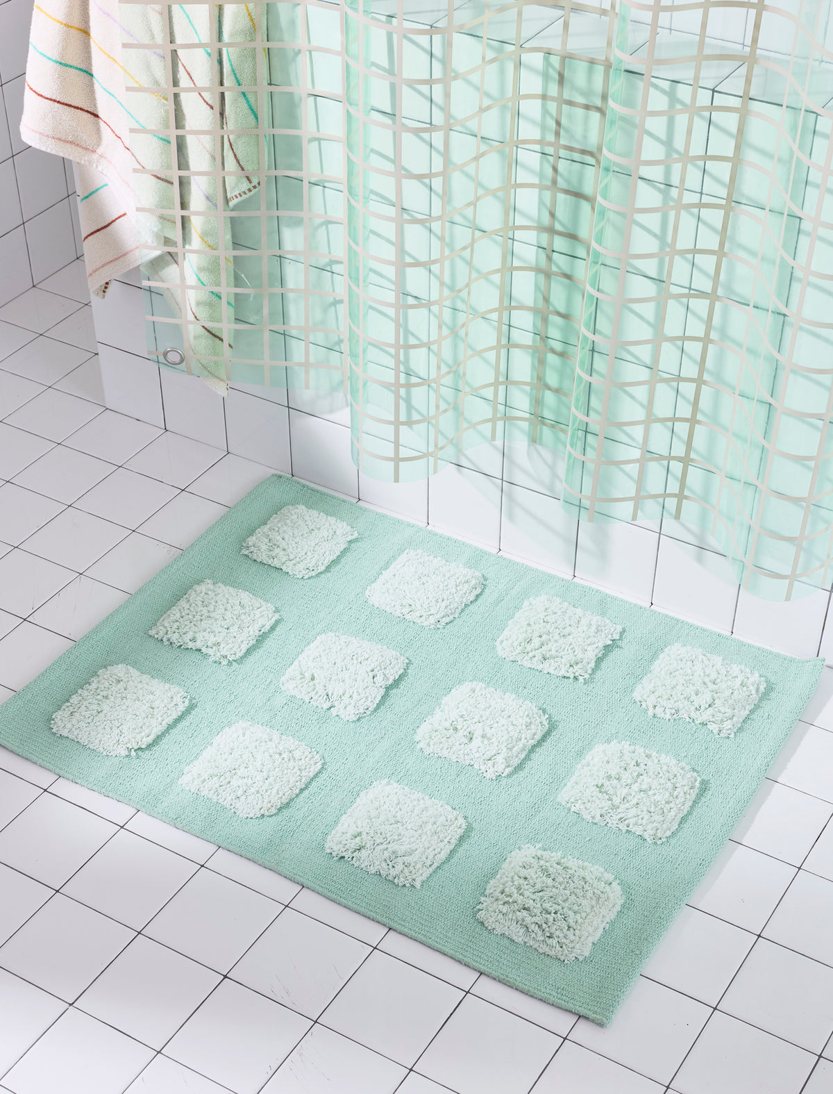 Mint/Teal bath rug with an organic grid of raised tufted squares, shown in a bright white tiled bathroom with a teal shower curtain.