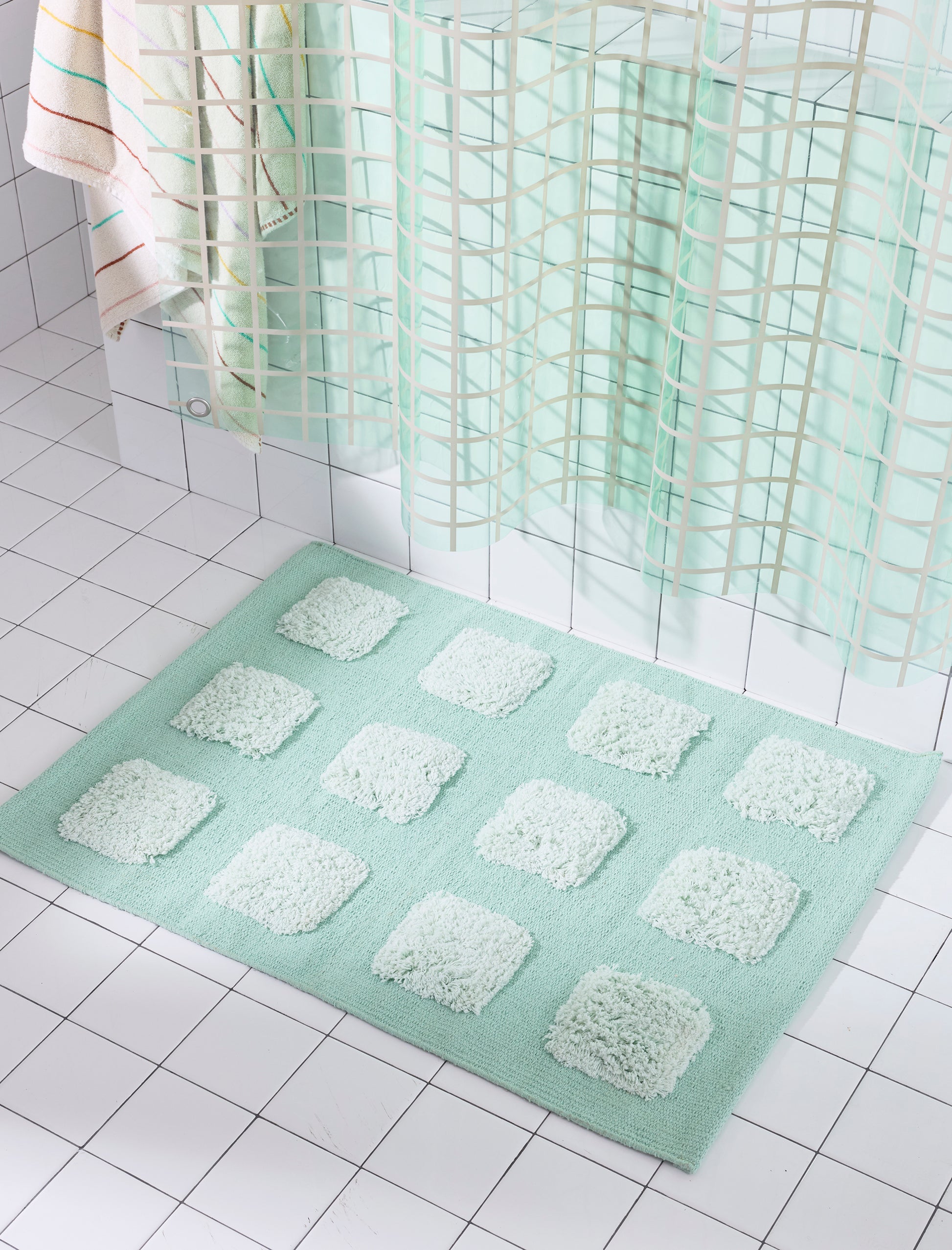 Mint/Teal bath rug with an organic grid of raised tufted squares, shown in a bright white tiled bathroom with a teal shower curtain.