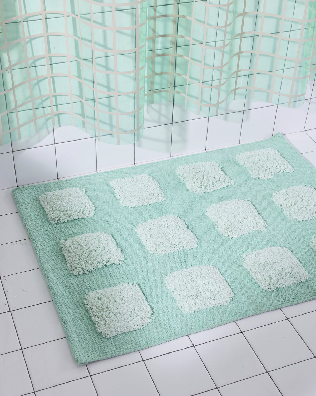 Mint/Teal bath rug with an organic grid of raised tufted squares, shown in a bright white tiled bathroom with a teal shower curtain.