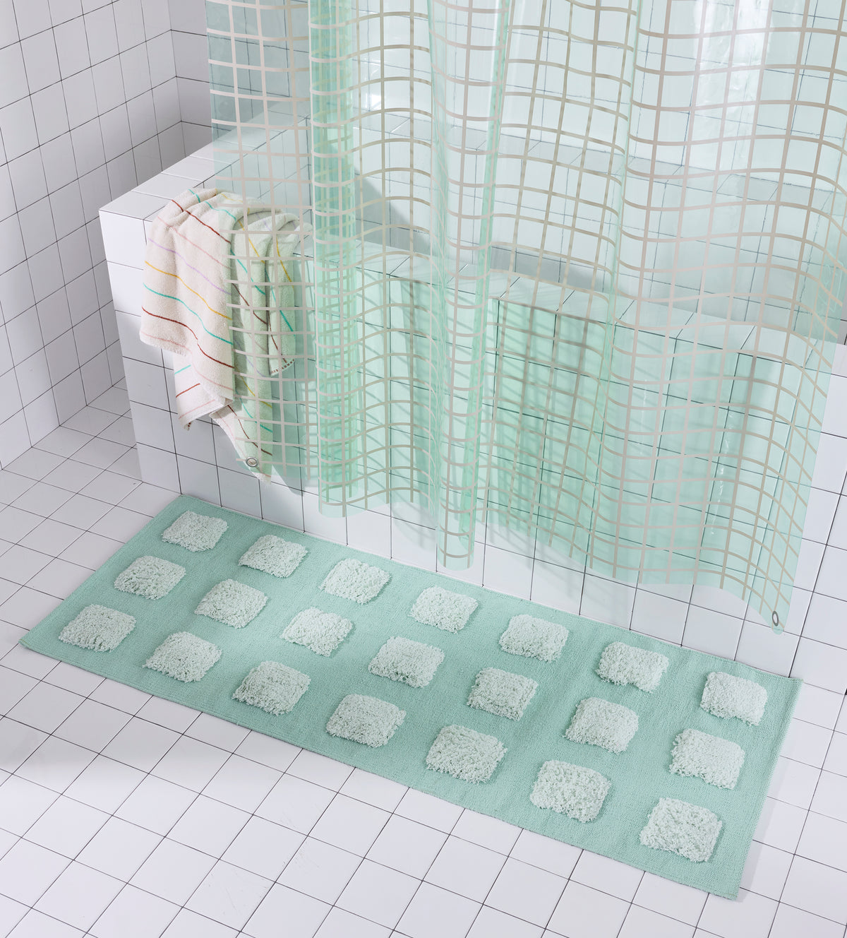 Mint/Teal bath runner with an organic grid of raised tufted squares, shown in a bright white tiled bathroom with a teal shower curtain.