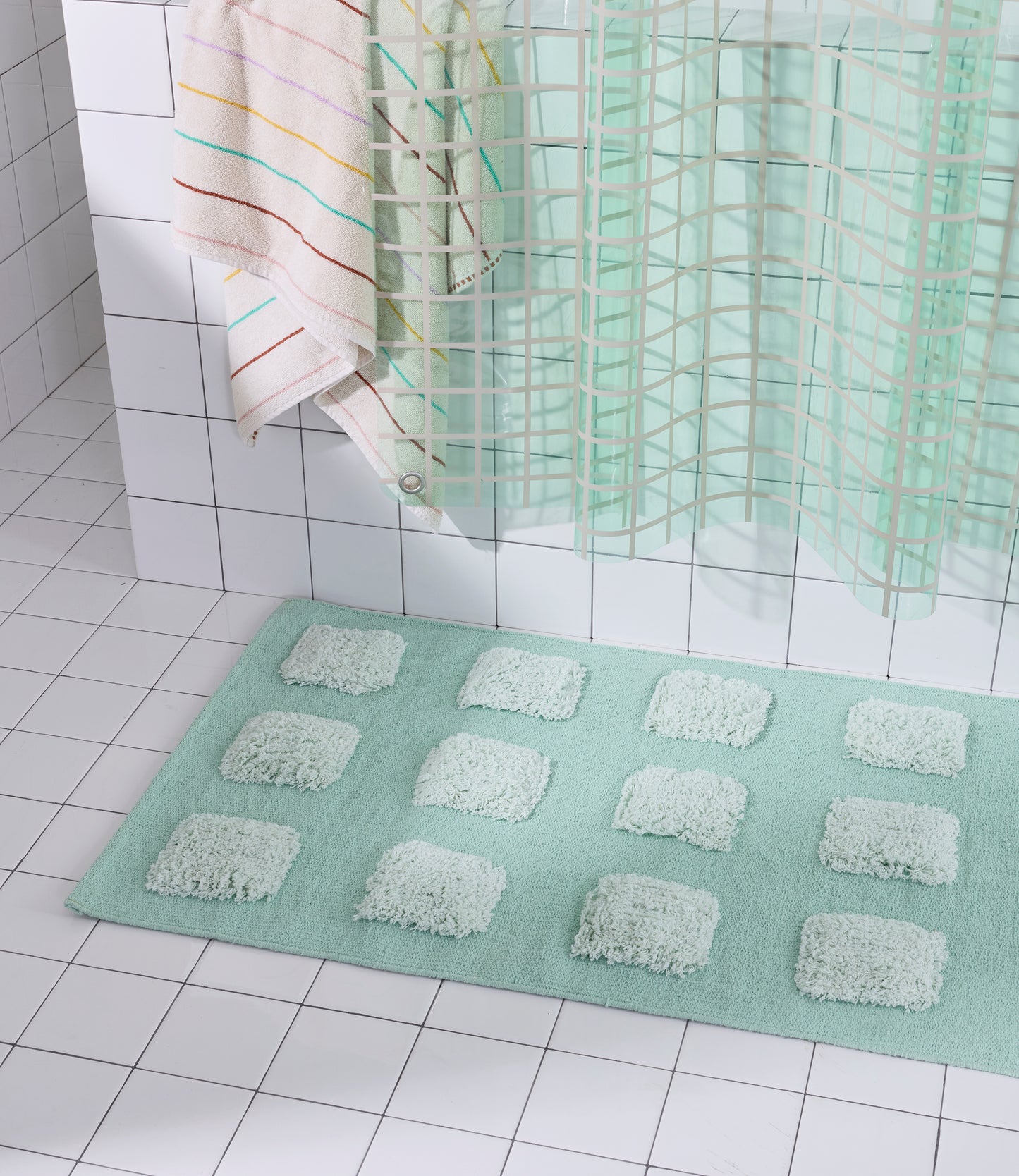 Mint/Teal bath rug with an organic grid of raised tufted squares, shown in a bright white tiled bathroom with a teal shower curtain.