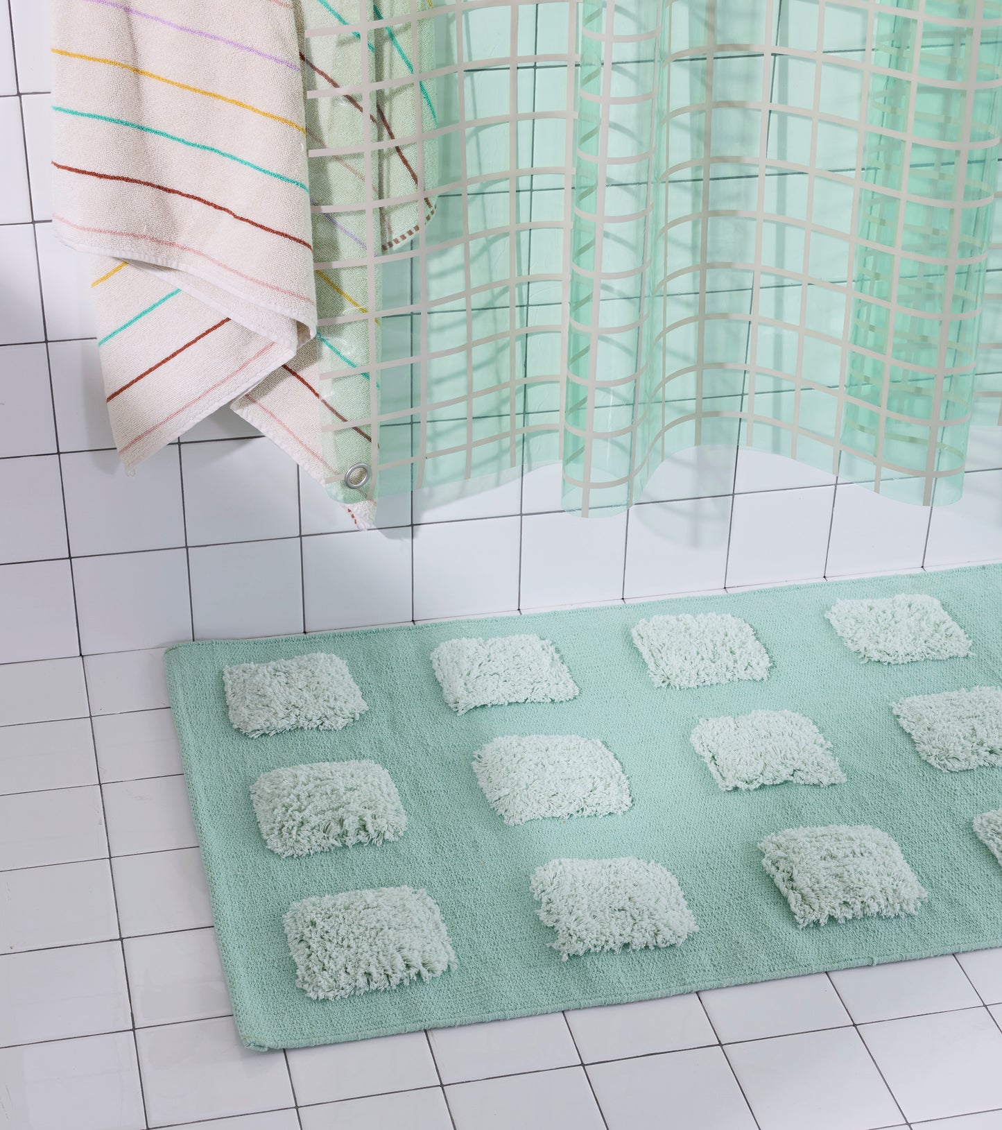Close-up of the Mint/Teal, natural bath runner showing its textured woven base and raised plush tufted squares beneath a teal shower curtain.