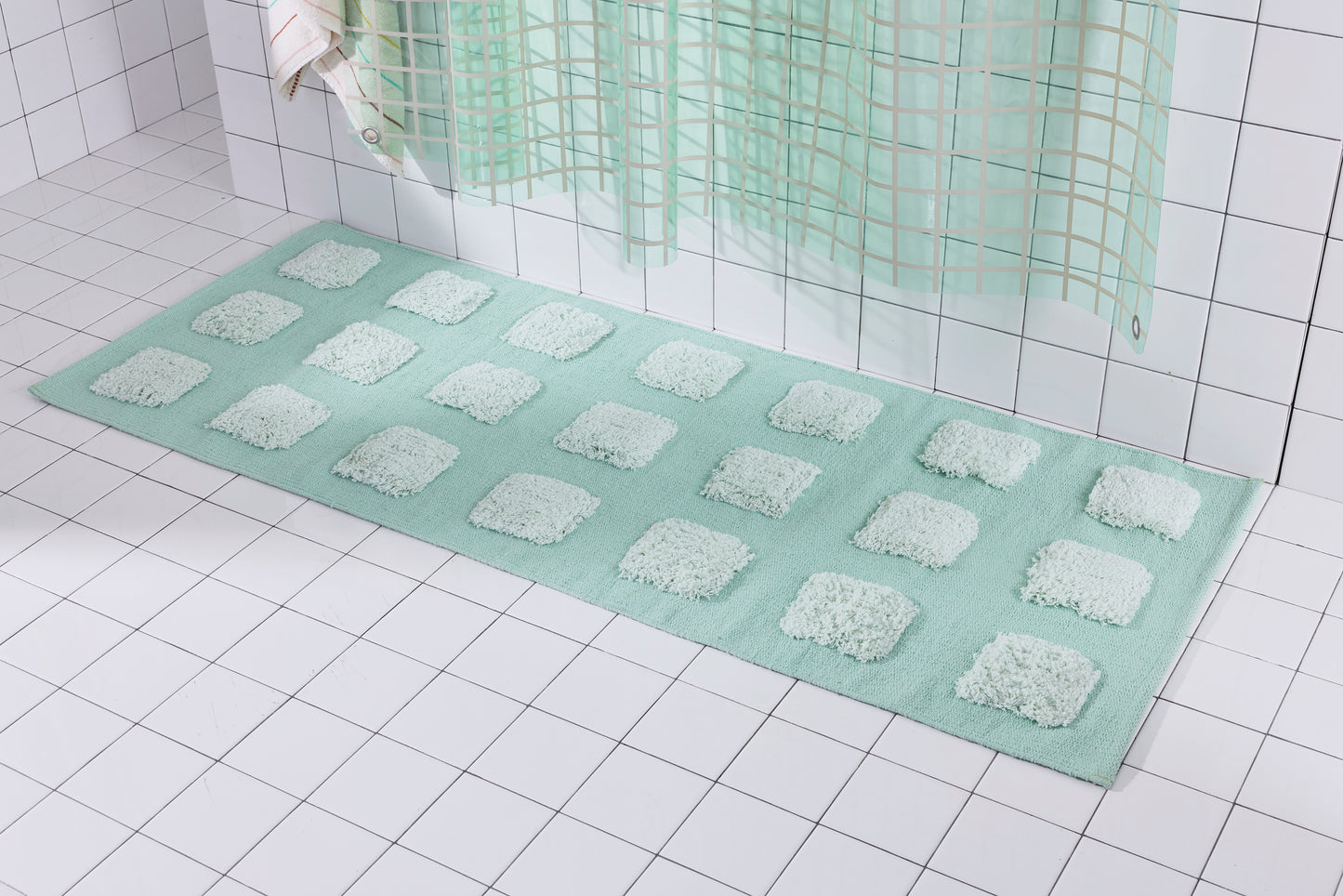 Mint/Teal bath runner with an organic grid of raised tufted squares, shown in a bright white tiled bathroom with a teal shower curtain.
