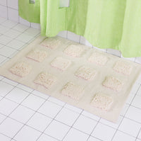 Cream rug with an organic grid of raised tufted squares, shown in a bright white tiled bathroom with a lime green shower curtain.