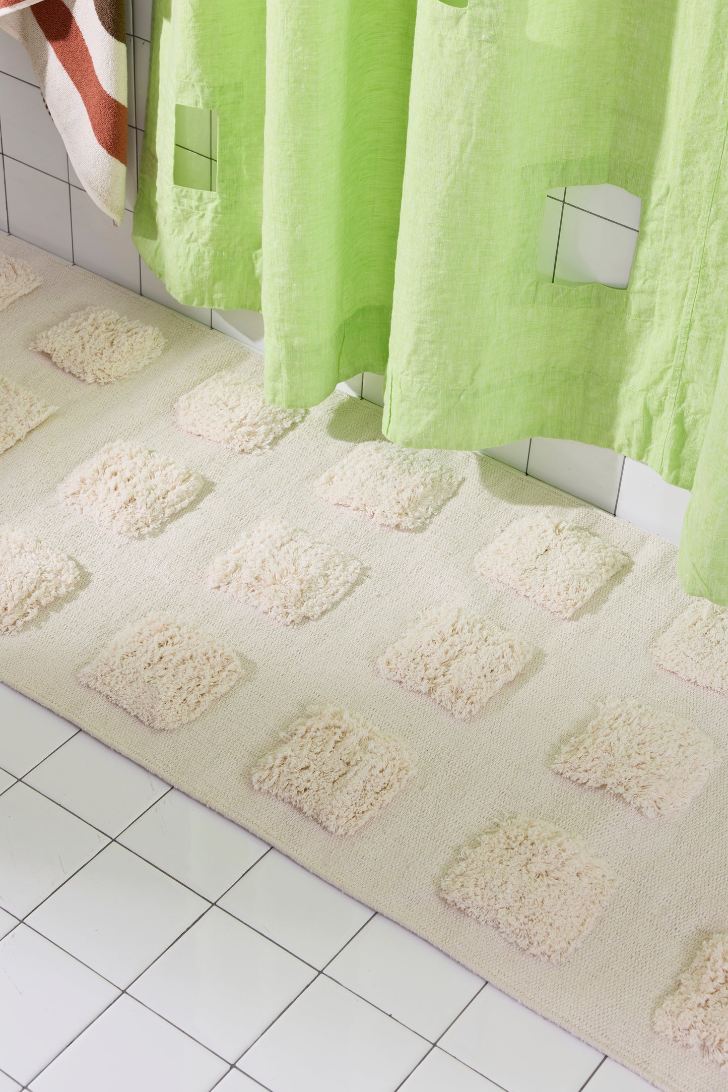 A close-up of Cream runner with an organic grid of raised tufted squares, shown in a bright white tiled bathroom with a lime green shower curtain.