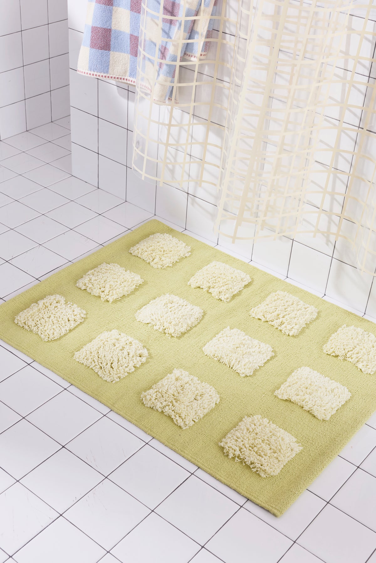 A yellow/olive natural woven bath mat featuring twelve raised, natural-colored textured rectangular tufts arranged in a 4-by-3 grid pattern.