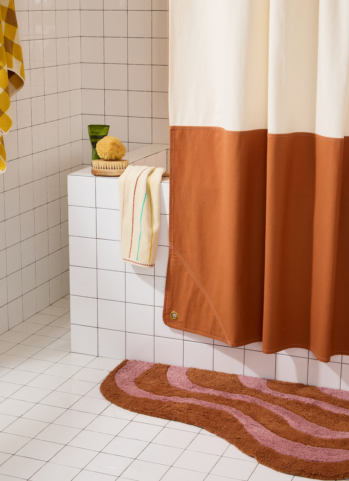 Orient clay shower curtain styled with a wavy bath rug, striped hand towel, and body care products.