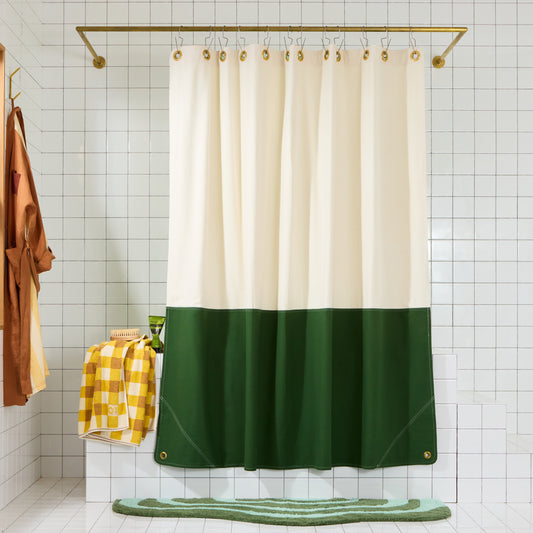 Full front view of Orient Pine colorblock shower curtain hanging on a brass rod in a white-tiled bathroom.
