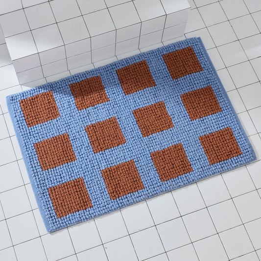 Rectangular Portal atlantic light blue woven bath mat with rust-brown square blocks, positioned against a white tile ledge.