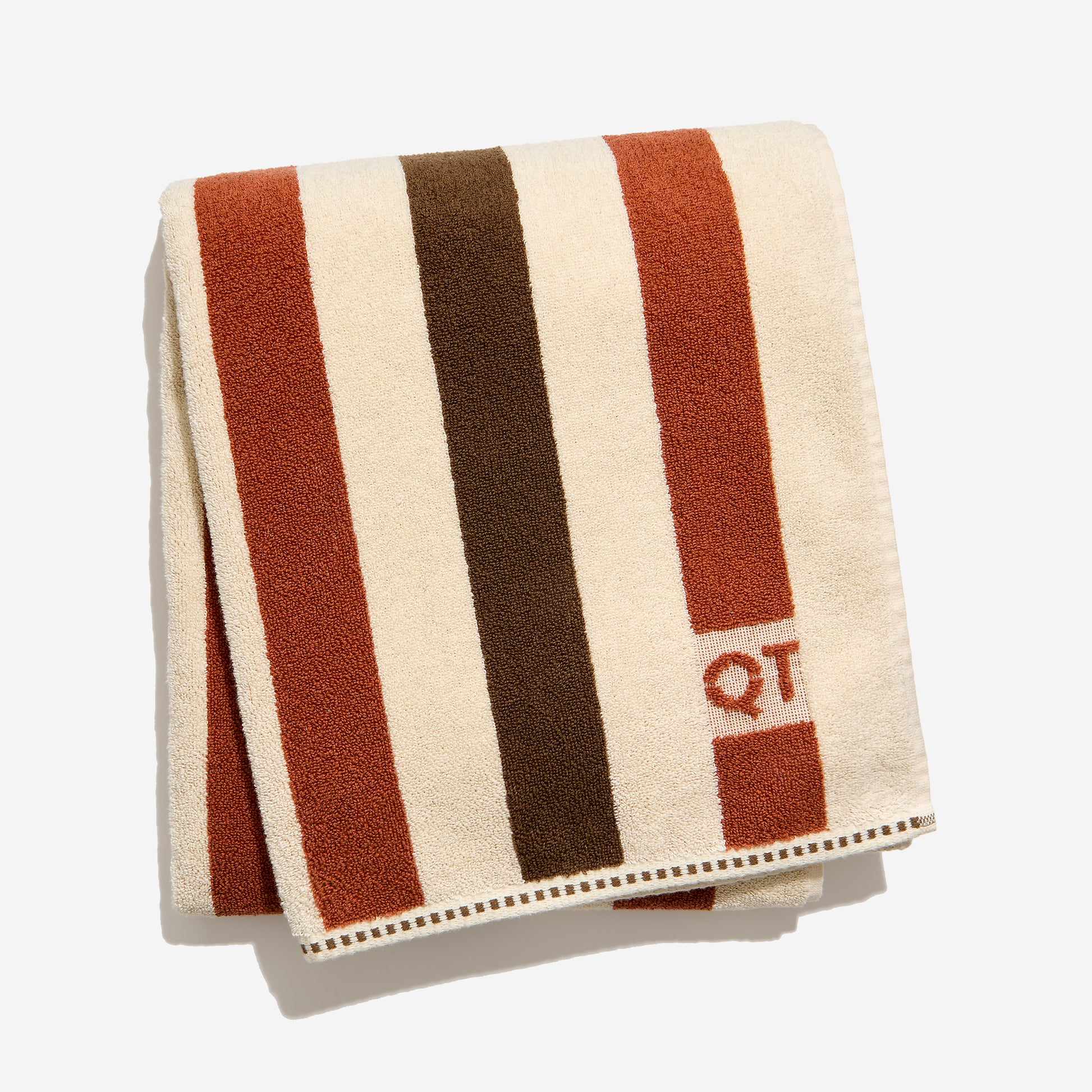 Striped towel with brown, clay, and cream colors and 'QT' logo on a white background