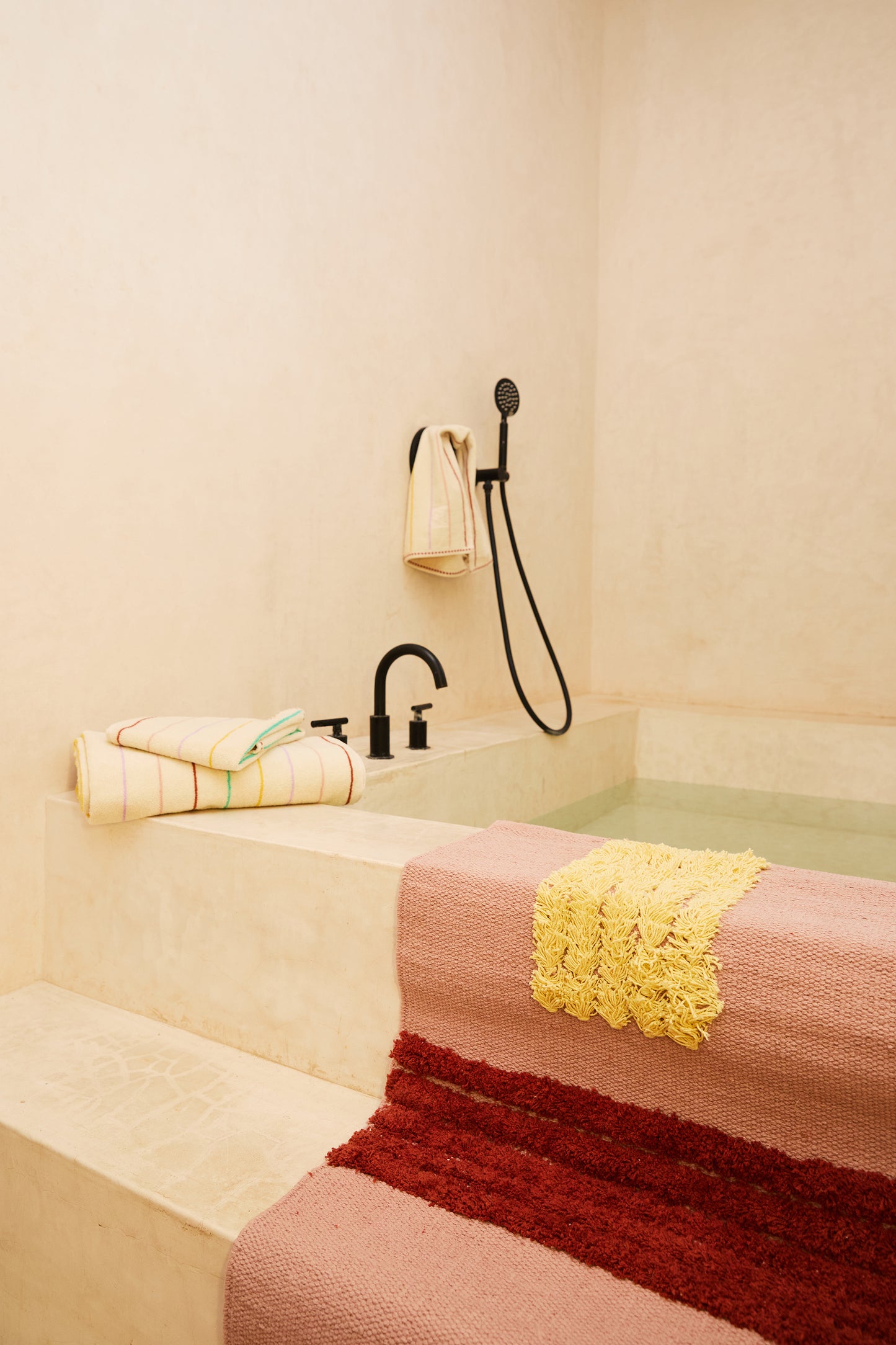 rose colored reyes rug over steps leading into bath tub styled with striped towels. 