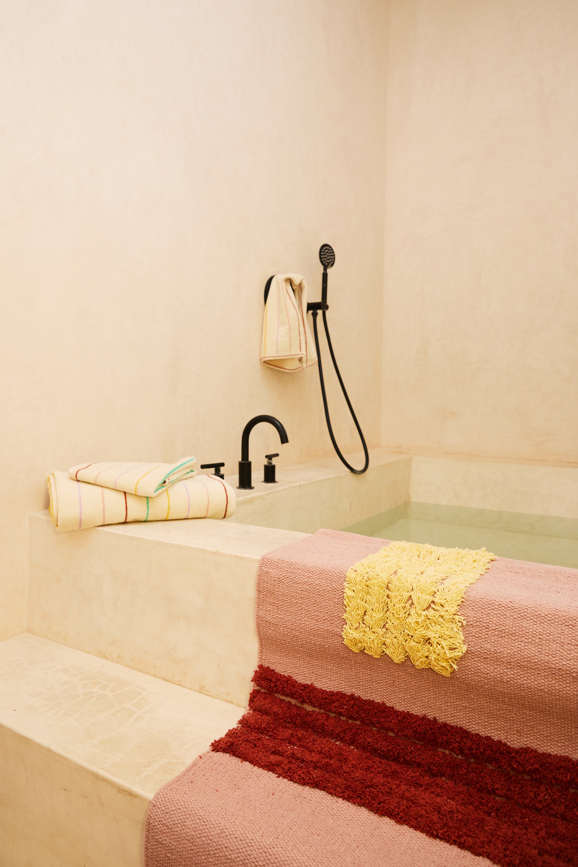 rose colored reyes rug over steps leading into bath tub styled with striped towels. 