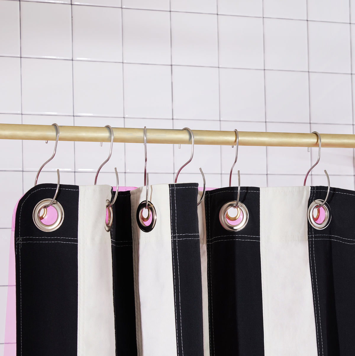 Black and white striped shower curtain with metal grommets hanging from a gold rod against a white tiled wall.
