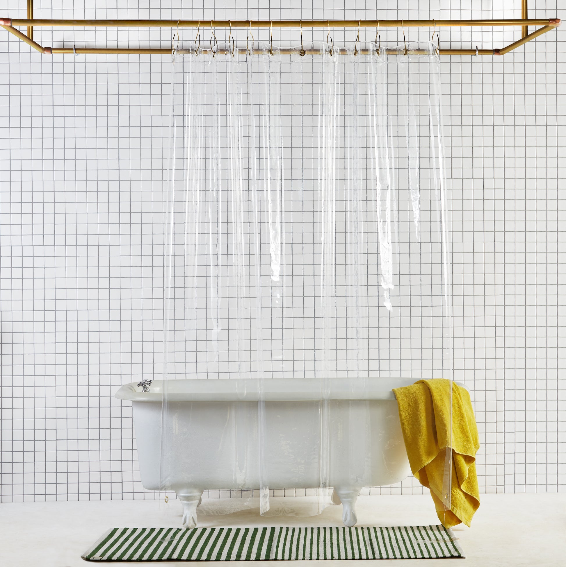 Sun shower curtain in air hanging over bathtub styled in a white tiled bathroom 