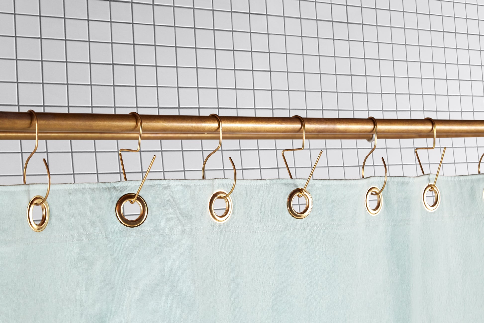 mint green curtain with brass grommets hanging from brass hooks